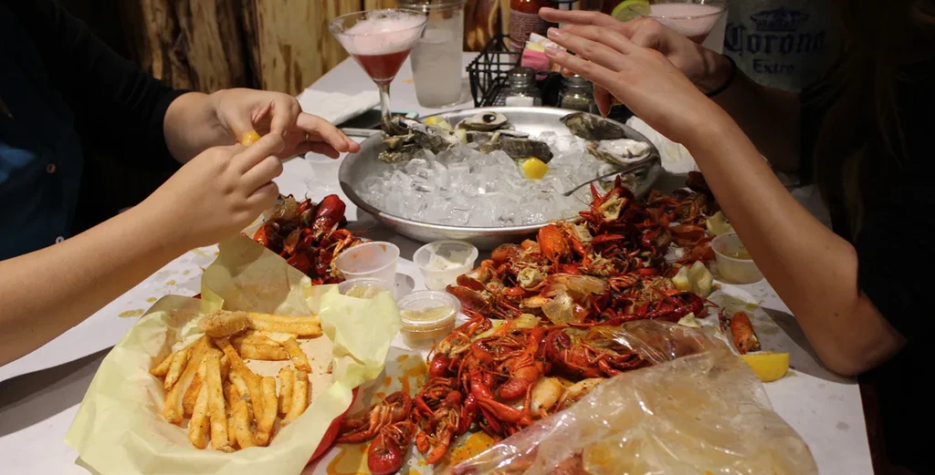 Hands eating a large seafood meal of oysters, crawfish, and fries.