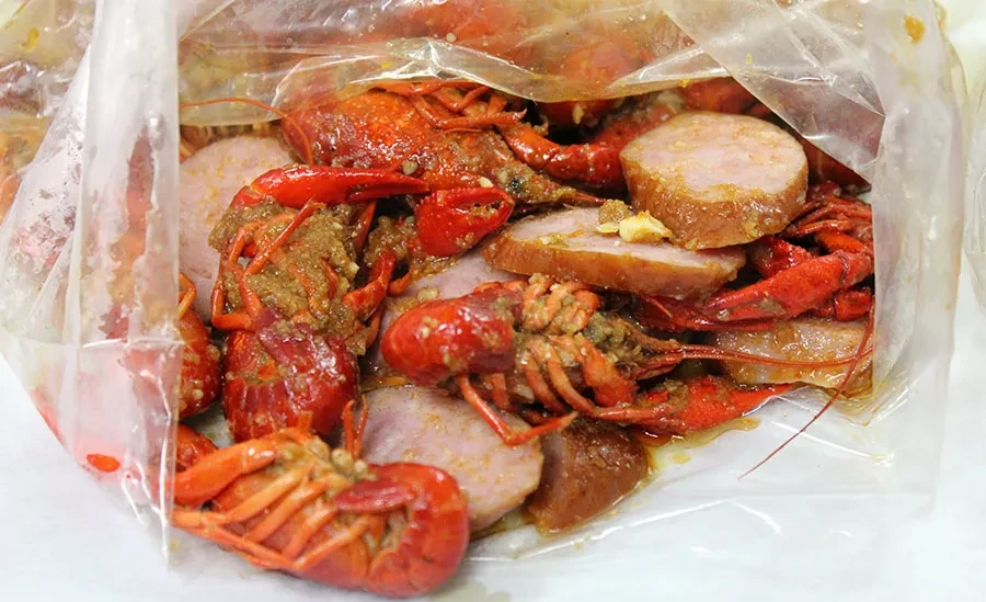 Crawfish and sausage seafood boil, sauced in a clear plastic bag.