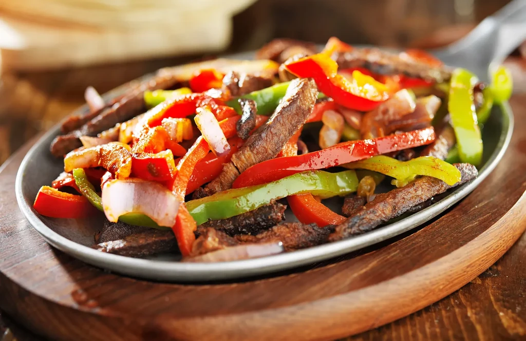 Sizzling beef fajitas with colorful peppers and onions on a wooden board.