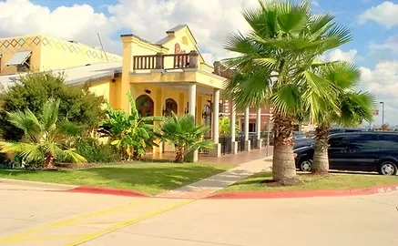 Vibrant yellow building with balcony, white columns, and palm trees.