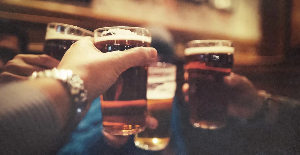 Hands clinking frothy amber beer glasses in a warm toast.