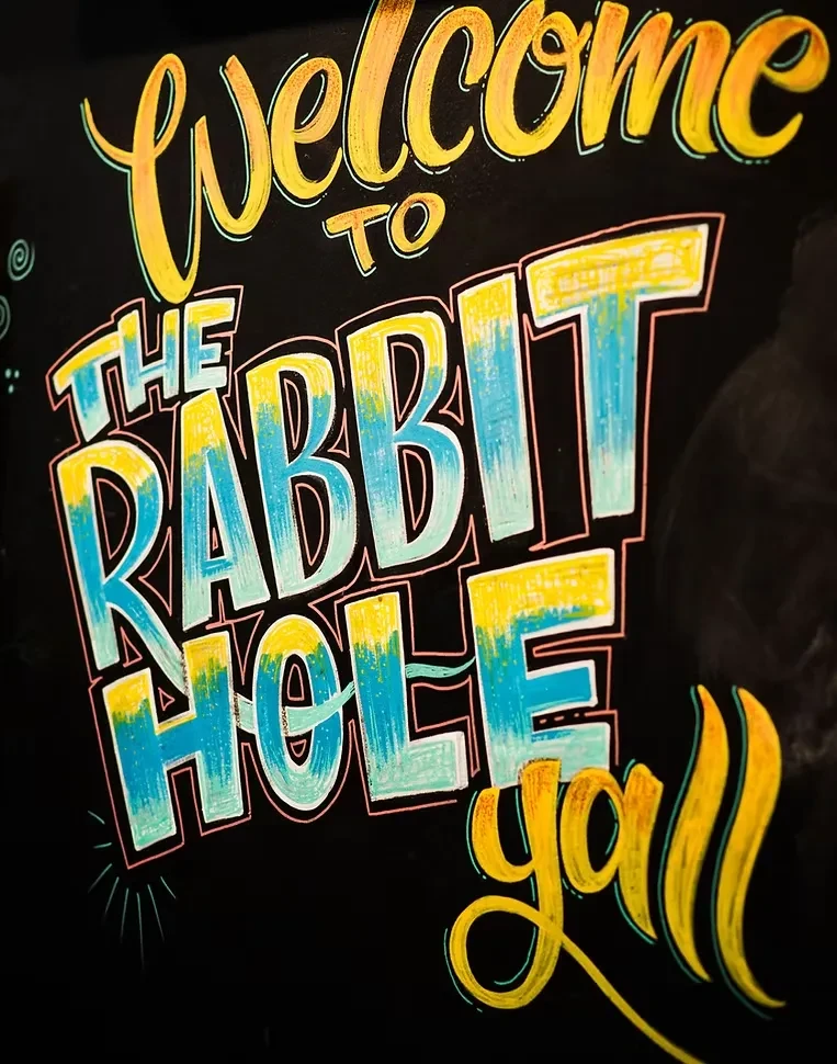 Hand-lettered chalkboard sign says 'Welcome TO THE RABBIT HOLE y'all'.