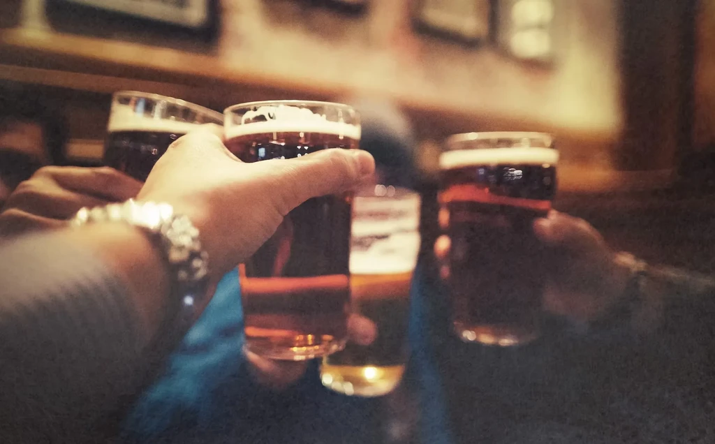 Hands clinking beer glasses in a dimly lit bar.