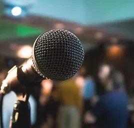 Dynamic microphone on stand; blurred audience and warm lights behind.