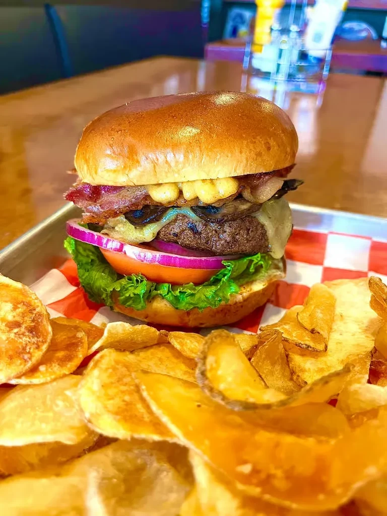 Tall burger with mac and cheese, bacon, and potato chips.