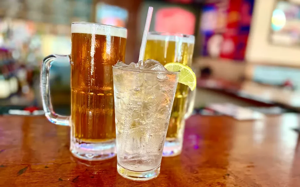 A bubbly drink with lime and two beers on a wooden bar.