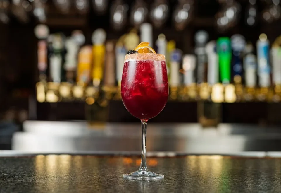 Garnished red drink in a stemmed glass on a bar.