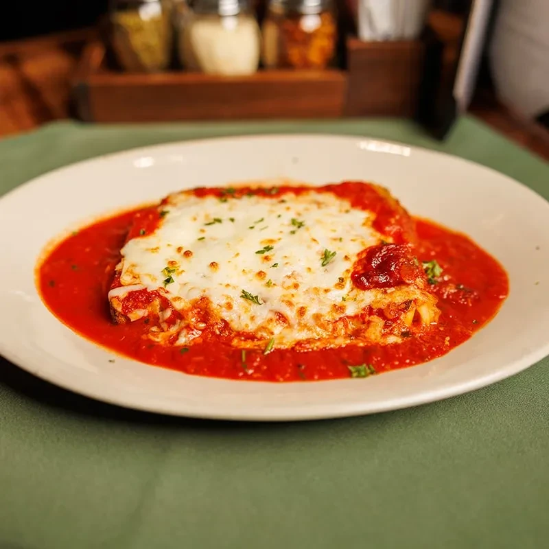 Baked pasta dish with melted cheese, tomato sauce, and green herbs.