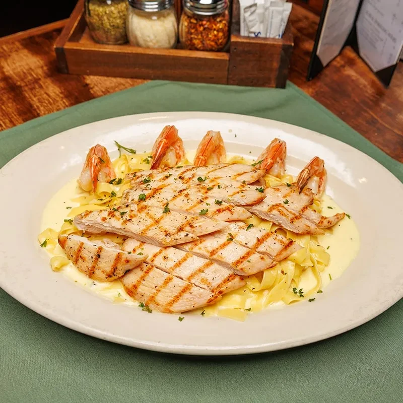 Creamy fettuccine pasta, grilled chicken, and shrimp garnished with herbs.