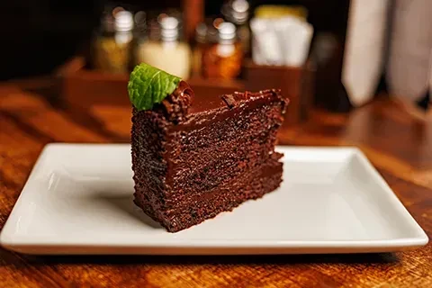A layered chocolate cake slice with thick frosting and a mint leaf.