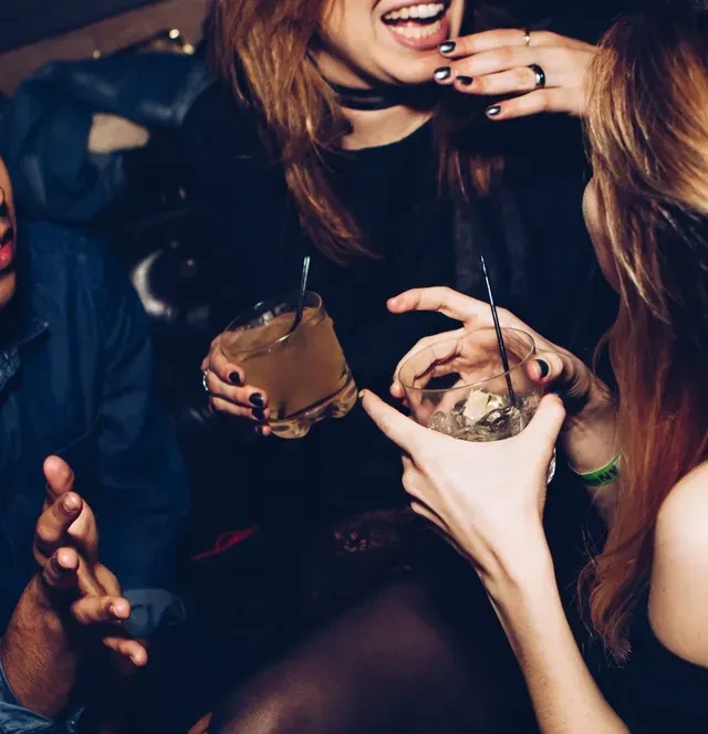 Hands and drinks of three people laughing in a dim bar.