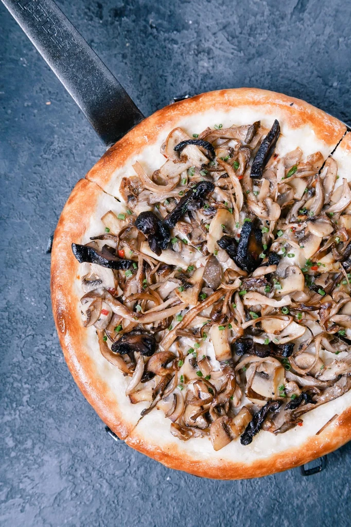 Close-up mushroom, onion, and herb flatbread in a dark pan.