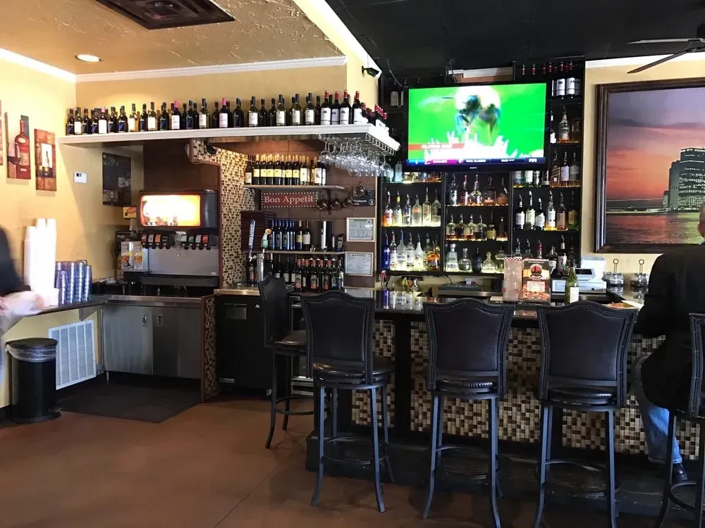Restaurant bar interior with stocked bottles, sports TV, and two people.