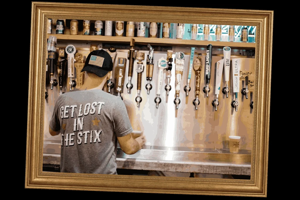 Back of person with 'GET LOST IN THE STIX' shirt facing beer taps.