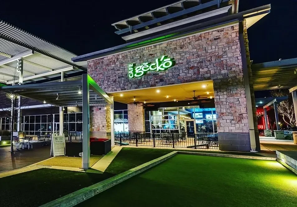 Night view of Cafe Gecko with green neon sign and turf bocce court.