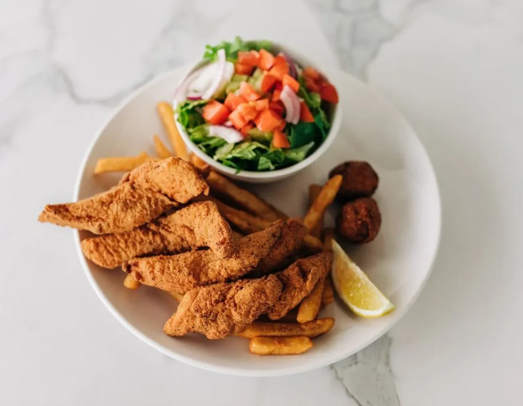 Fried fish, french fries, green salad, and lemon on a white plate.