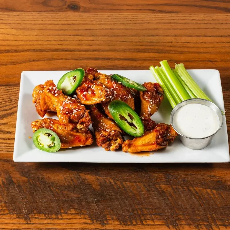Buffalo chicken wings with sesame, jalapeños, celery, and dip on wood.