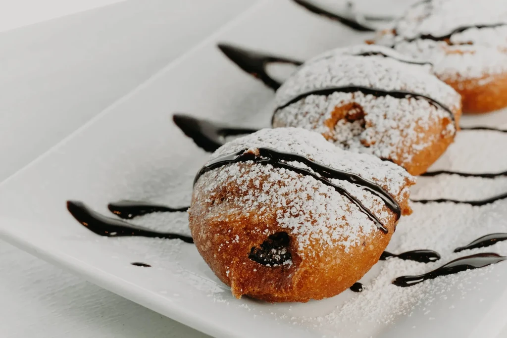 Three golden pastries with powdered sugar and chocolate drizzle.