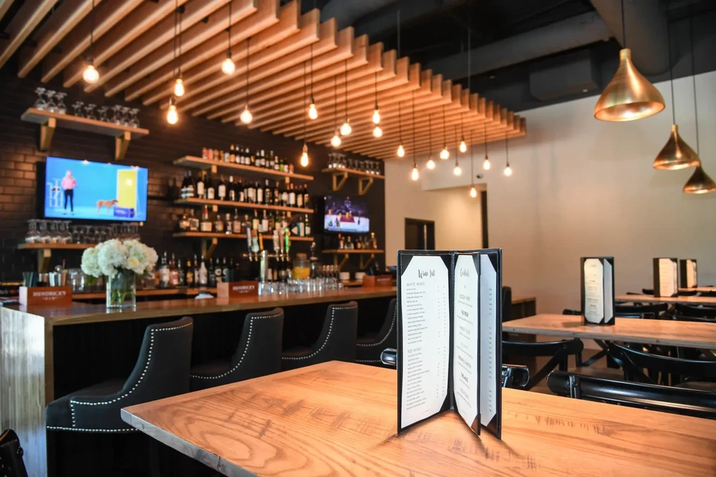 Modern restaurant bar with menus, liquor, and Edison lighting.