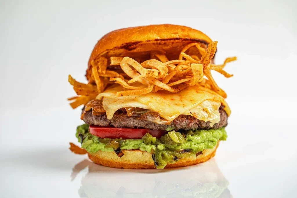 Gourmet burger on brioche bun with beef, cheese, guacamole, crispy strips.