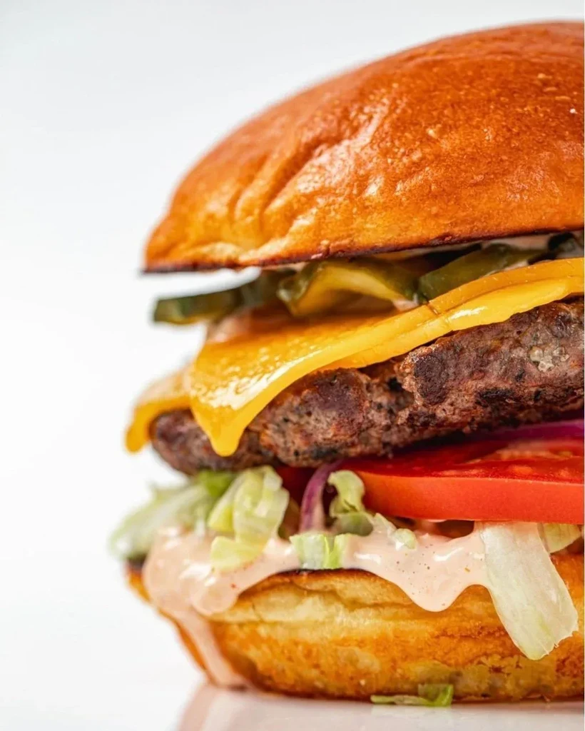 Side-profile burger with beef, melted cheese, lettuce, tomato, and dripping sauce.