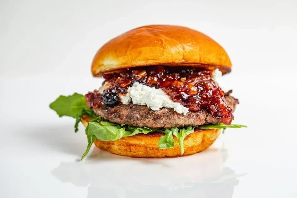 A gourmet burger with beef, brioche, arugula, cheese, and berry compote.