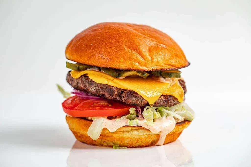 Hamburger with brioche bun, beef patty, melted cheese, fresh vegetables, pink sauce.