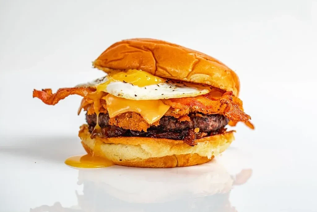 Gourmet beef burger with bacon, cheese, hash brown, and runny fried egg.