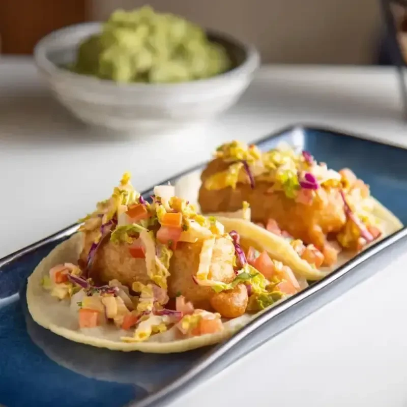 Two crispy fish or shrimp tacos topped with vibrant slaw.