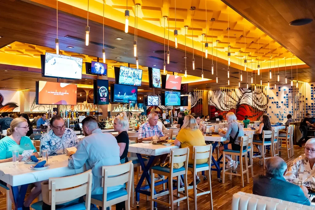 Bustling modern restaurant/bar interior with Edison bulbs, TVs, bar.