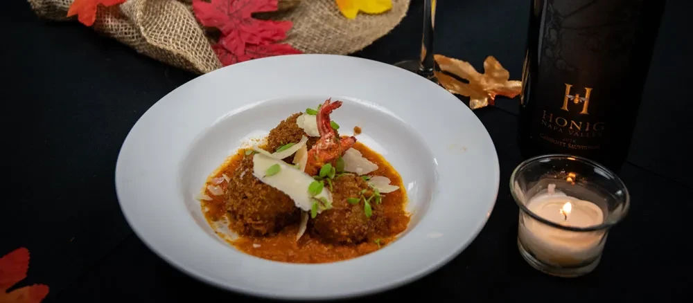 Plated deep-fried dish in sauce with Parmesan, wine, and autumn decor.