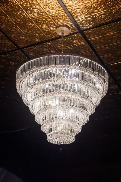 Large multi-tiered crystal chandelier hanging from a patterned gold ceiling.
