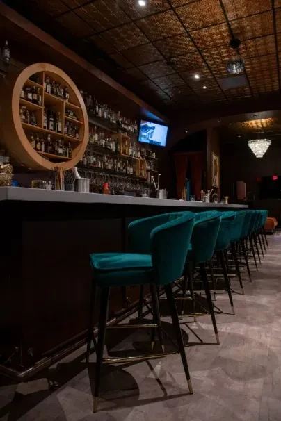 Upscale bar interior, teal stools, marble counter, extensive liquor display.