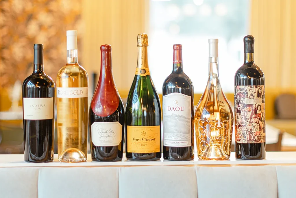 Seven diverse wine and champagne bottles displayed horizontally on a light surface.