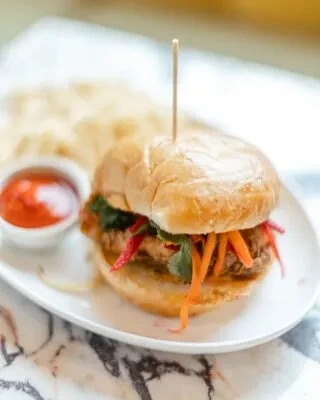 Crispy fried chicken sandwich with vegetables, herbs, red sauce, and chips.