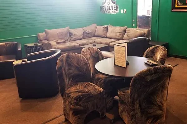 Revolver Brewing lounge with green wall, brown sectional, and patterned chairs.