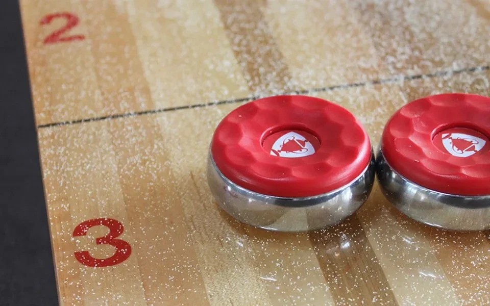 Two red shuffleboard pucks on a powdered table with scoring numbers.