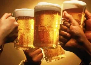Multiple hands toast three amber beers with white foam.