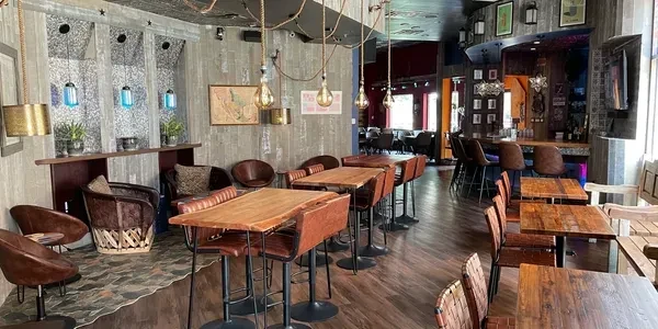 Empty, eclectic restaurant interior with wooden tables, industrial lighting, and a bar.