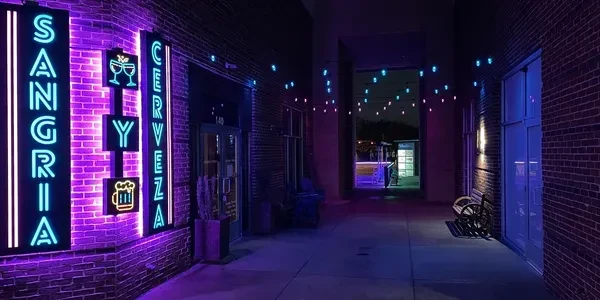 Vibrant neon signs for "Sangria y Cerveza" light a dark restaurant entrance.
