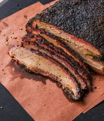 Sliced smoked brisket with dark bark, pink interior, and smoke ring.