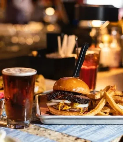 Burger with knife, fries, and dark beer in restaurant setting.
