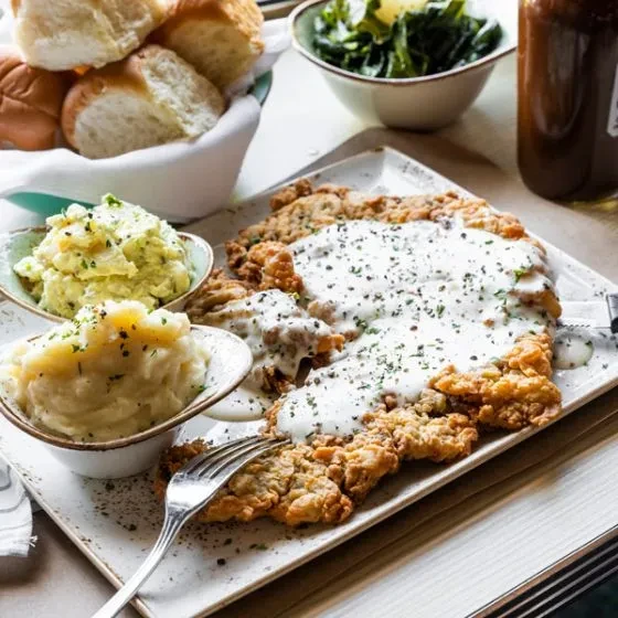 Crispy chicken fried steak with gravy, mashed potatoes, and bread rolls.