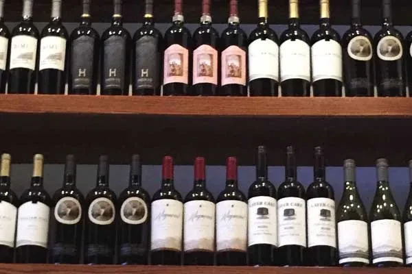 Two wooden shelves holding rows of diverse wine bottles.