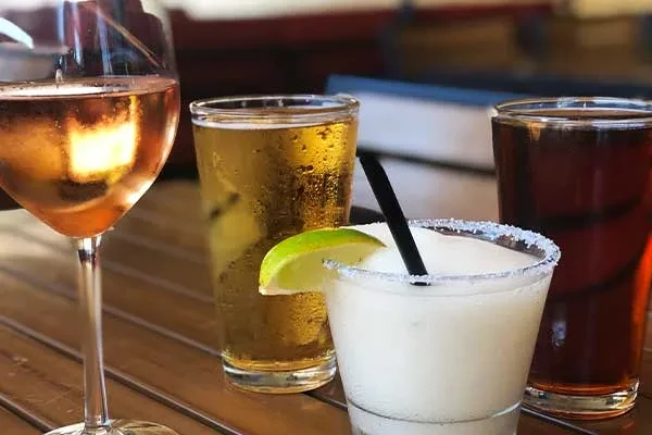 Close-up: Four cold drinks (rosé, beer, margarita, dark) on wood table.