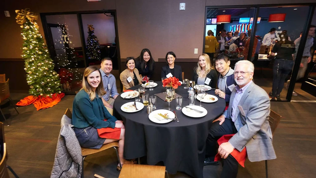 Eight smiling people at a table in a holiday-decorated Pinstack venue.