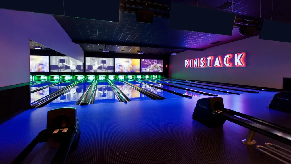Pinstack bowling alley with blue and green LED-lit lanes and screens.