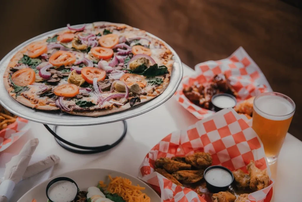 Vegetable pizza, chicken wings, beer, salad, and fries.