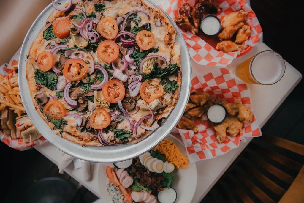 Overhead view of a pizza, wings, beer, salad, and fries.