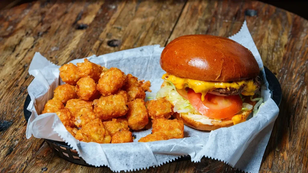Cheeseburger with melted cheese, crispy tater tots on a wooden table.